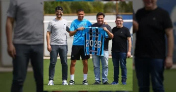 Foto de Alysson, atacante do Grêmio, ao lado de representantes do clube, segurando uma camisa com seu nome e o ano 2029, símbolo da renovação de contrato. Créditos ao Grêmio.